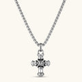 Sterling silver cross pendant with cylindrical arms, floral center medallion, and engraved emblem, shown solo and on a box chain.