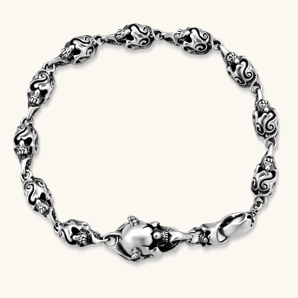 Sterling silver bracelet with linked skull motifs, decorative scroll engravings, and a large skull lobster-claw clasp.